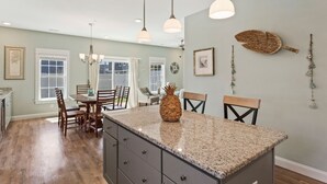 A kitchen with a granite countertop, wooden chairs, and pendant lights. - Charming 3-Bed Townhome Steps from the Beach (Kill Devil Hills)