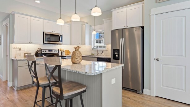 A modern kitchen with white cabinets, stainless steel appliances, and a central island with bar stools. - Charming 3-Bed Townhome Steps from the Beach (Kill Devil Hills)