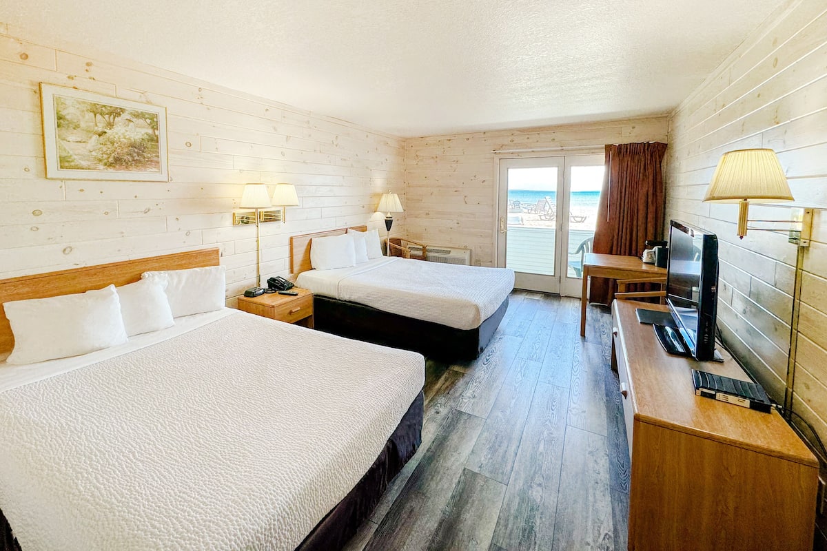 Habitación de hotel con dos camas, un escritorio, un televisor y vista a la playa.