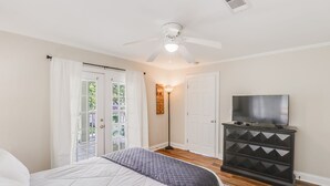 A bedroom with a bed, a ceiling fan, a TV on a dresser, and a view of the outdoors through a glass door.