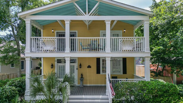 A two-story yellow house with a balcony, a porch, and a small garden.