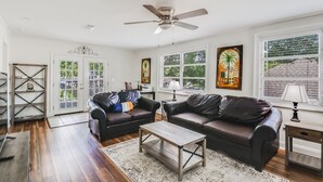 A living room with two dark leather sofas, a wooden coffee table, and a ceiling fan.