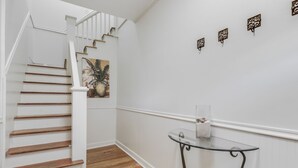 A staircase with wooden steps and white railings, a glass table with a vase, and decorative wall art.