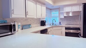 A modern kitchen with white cabinets, a stainless steel refrigerator, a microwave, and a coffee maker.