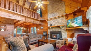 A cozy cabin interior with a stone fireplace, wooden furniture, and a ceiling fan. - Burning Tree: Pet Friendly, Free Attraction Tickets, Hot Tub, Mtn View & Close to SKY MTN Park (Sevierville)