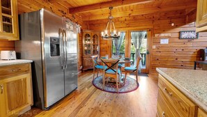 A wooden cabin kitchen with a stainless steel refrigerator, wooden cabinets, a dining table with chairs, and a chandelier. - Burning Tree: Pet Friendly, Free Attraction Tickets, Hot Tub, Mtn View & Close to SKY MTN Park (Sevierville)