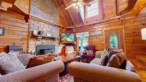 A cozy log cabin interior with a fireplace, comfortable seating, and a television. - Burning Tree: Pet Friendly, Free Attraction Tickets, Hot Tub, Mtn View & Close to SKY MTN Park (Sevierville)