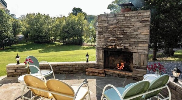 A stone fireplace with a fire, surrounded by outdoor seating. - Mountain Cottage: Pet Friendly, Free Attraction Tickets, Hot Tub, & In Wears Valley (Sevierville)