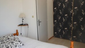A bedroom with a bed, a bedside table with a lamp, a wardrobe, and a floral-patterned door.