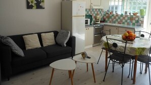 A compact living space with a kitchenette, a dining area with a table and chairs, and a sofa with cushions.