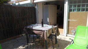 An outdoor patio with a table set for dining, surrounded by chairs, a green chair, and a wooden fence.