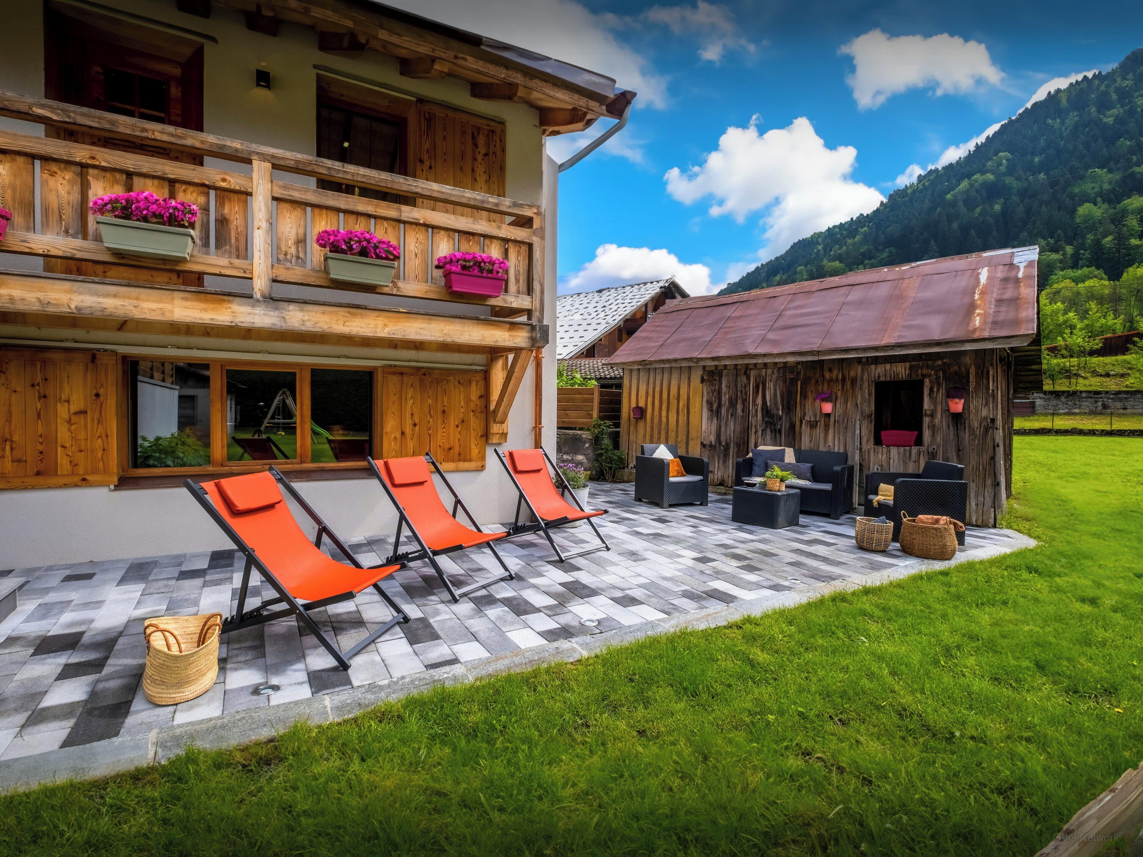 A chalet with a terrace, outdoor seating, and a mountain backdrop.