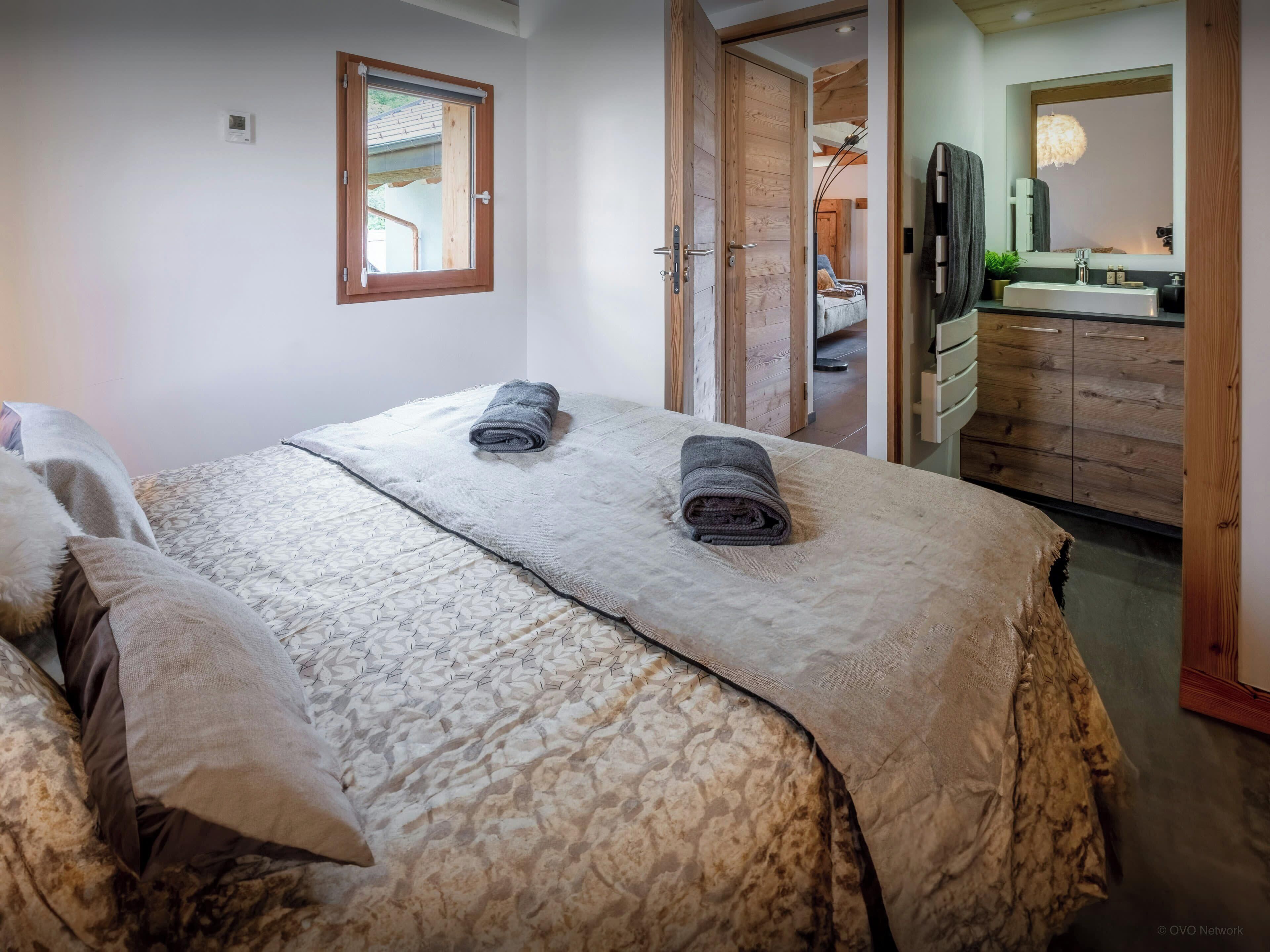 Une chambre à coucher avec un lit, deux serviettes, une fenêtre et une salle de bain visible à travers une porte ouverte.