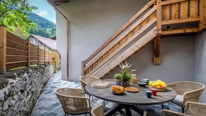 Un patio con una mesa redonda, sillas de mimbre y una escalera de madera.