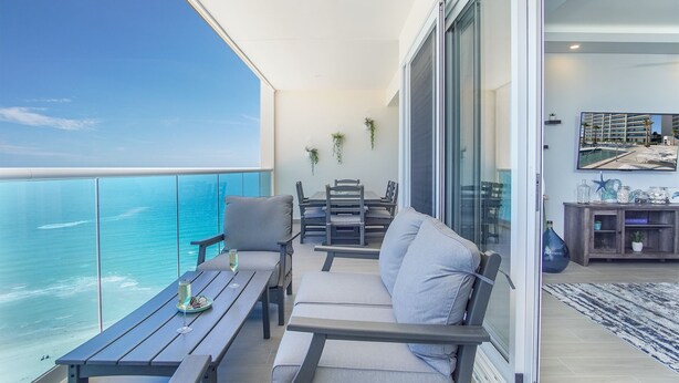 Een balkon met uitzicht op de oceaan, een eethoek met een tafel en stoelen, en een zithoek met een bank en salontafel.