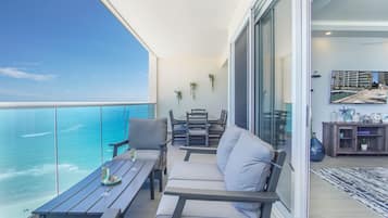 A balcony with a view of the ocean, a dining area with a table and chairs, and a living area with a sofa and a coffee table.