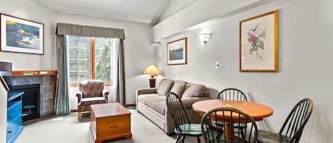 A cozy living room with a fireplace, a sofa, a dining table with chairs, and a television.