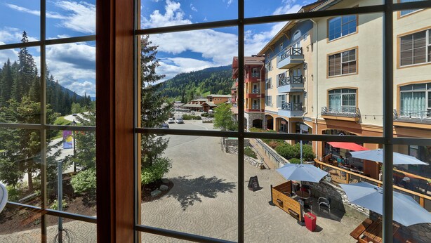Blick durch ein Fenster auf einen Innenhof mit Pflasterung, Außenbestuhlung und einem Berg im Hintergrund.