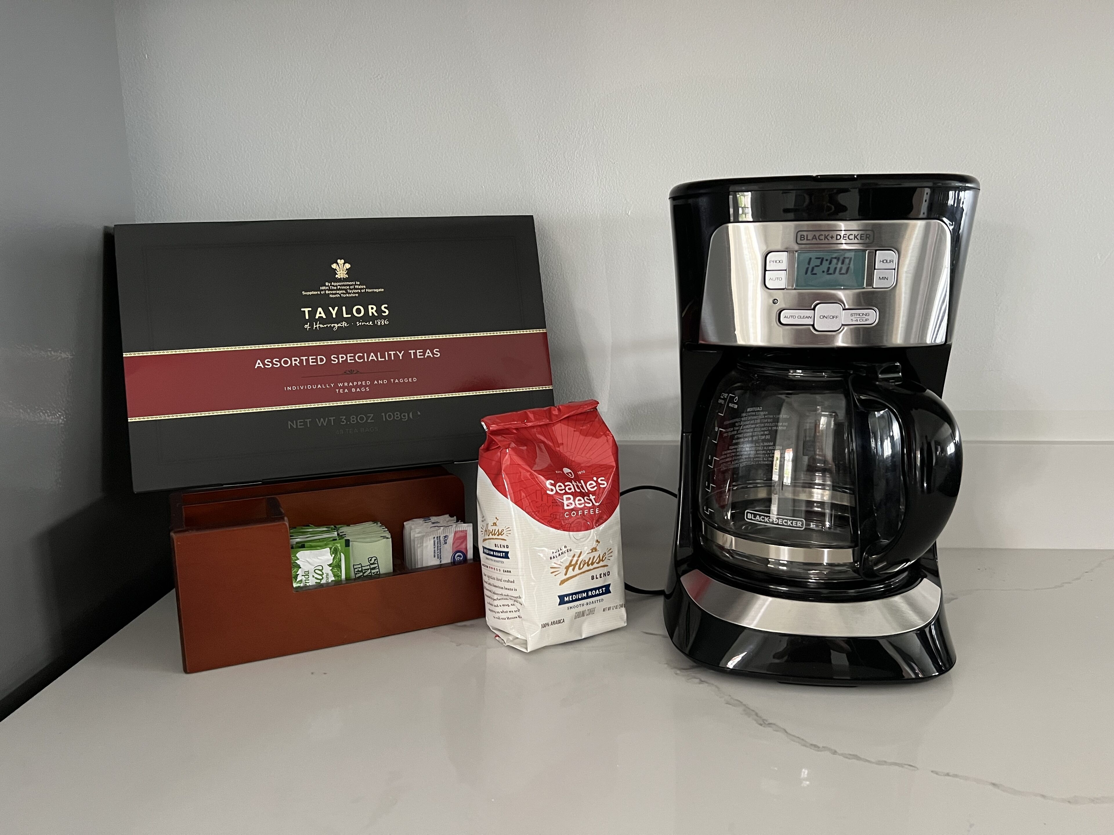 A coffee maker, a box of Taylor's specialty teas, and a bag of Sienna's Best Coffee blend.