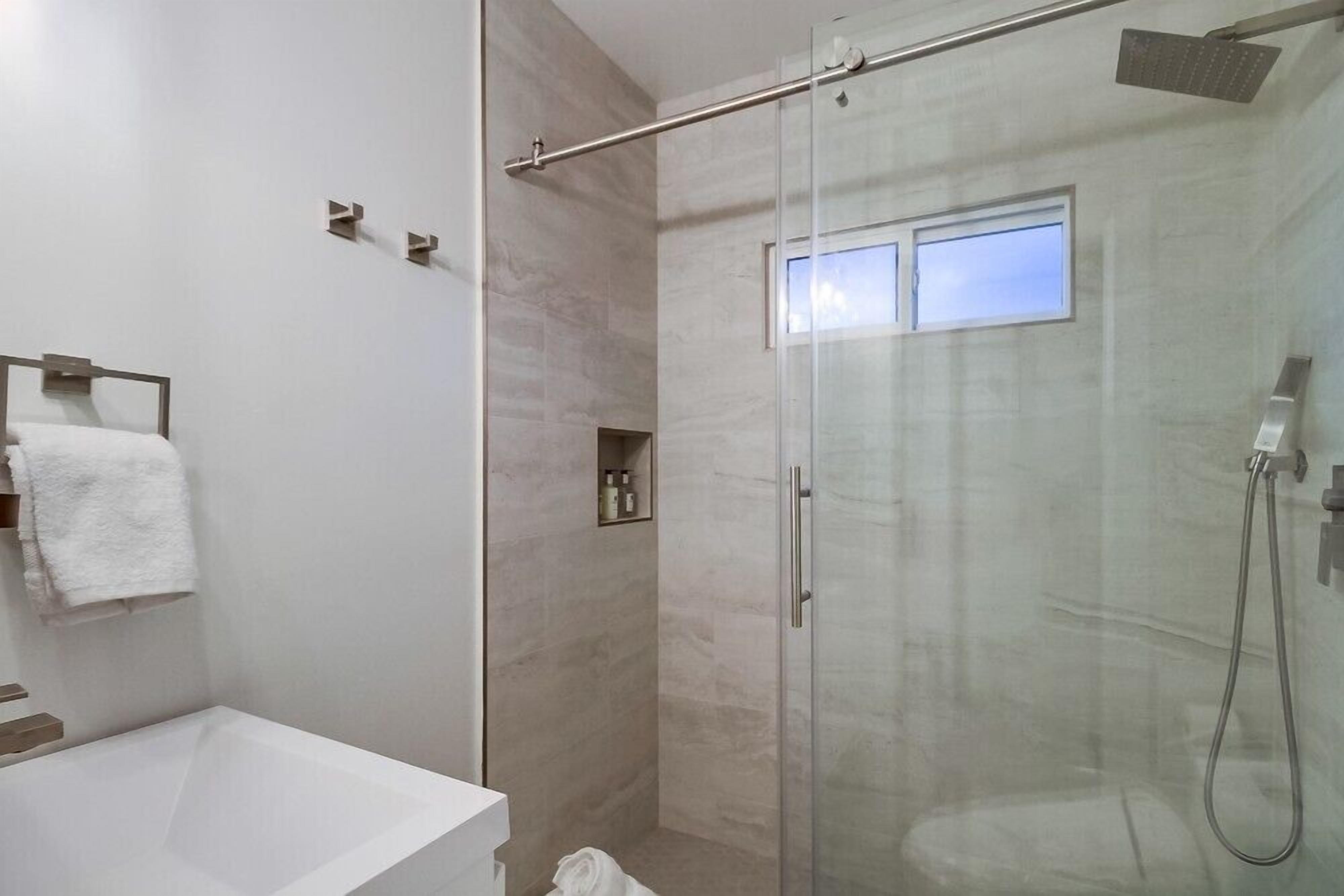 A modern bathroom with a glass-enclosed shower, a white bathtub, and a small shelf with toiletries.