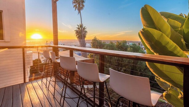 Eine Holzterrasse mit Barhocker und Blick auf den Sonnenuntergang über einer Stadtlandschaft.