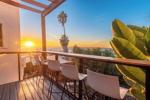 A wooden deck with bar stools and a view of the sunset over a cityscape.