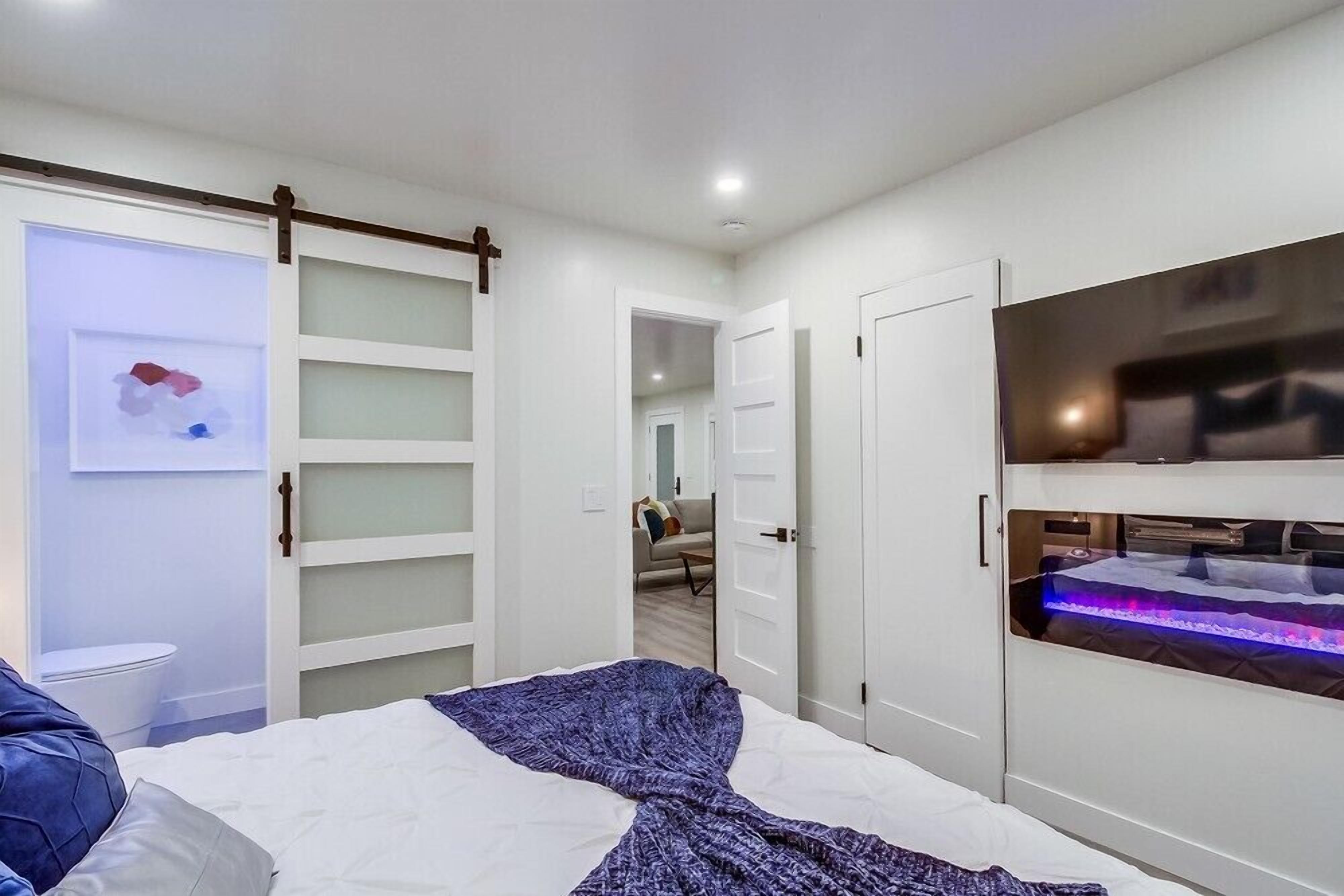 Een moderne slaapkamer met een bed, een schuifdeurkast, een aan de muur bevestigde televisie, en een badkamer op de achtergrond.