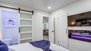 Een moderne slaapkamer met een bed, een schuifdeurkast, een aan de muur bevestigde televisie, en een badkamer op de achtergrond.