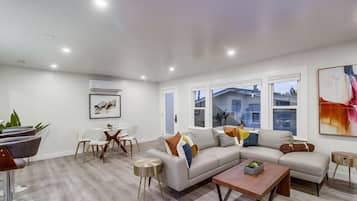 A modern living room with a sectional sofa, a coffee table, and a dining area with chairs and a small table.