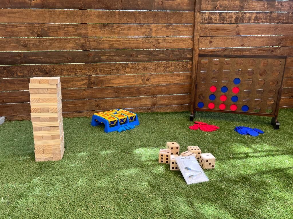 Een houten hek, een Jenga-toren, een Monopoly-bord en dobbelstenen op kunstgras.