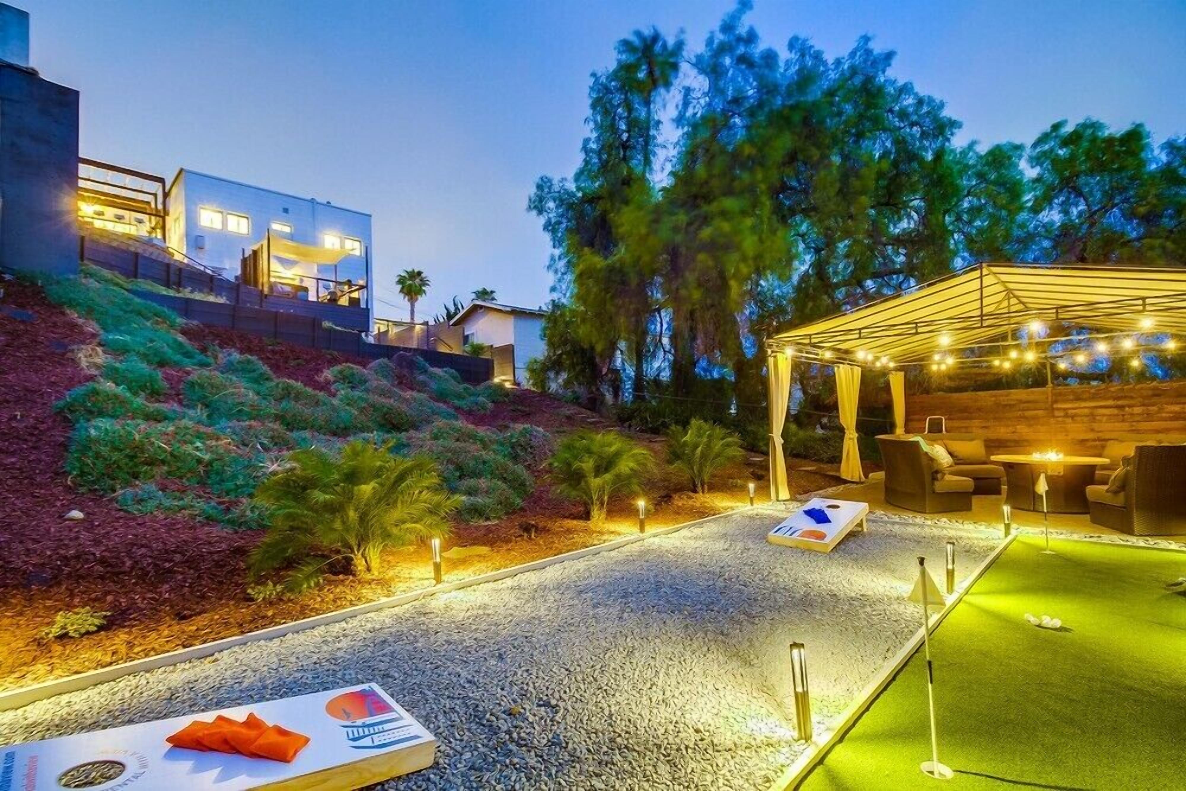 A well-lit outdoor area with a putting green, seating, and a covered area with string lights.