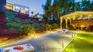 A well-lit outdoor area with a putting green, seating, and a covered area with string lights.