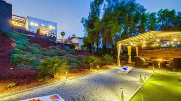 A well-lit outdoor area with a putting green, seating, and a covered area with string lights.