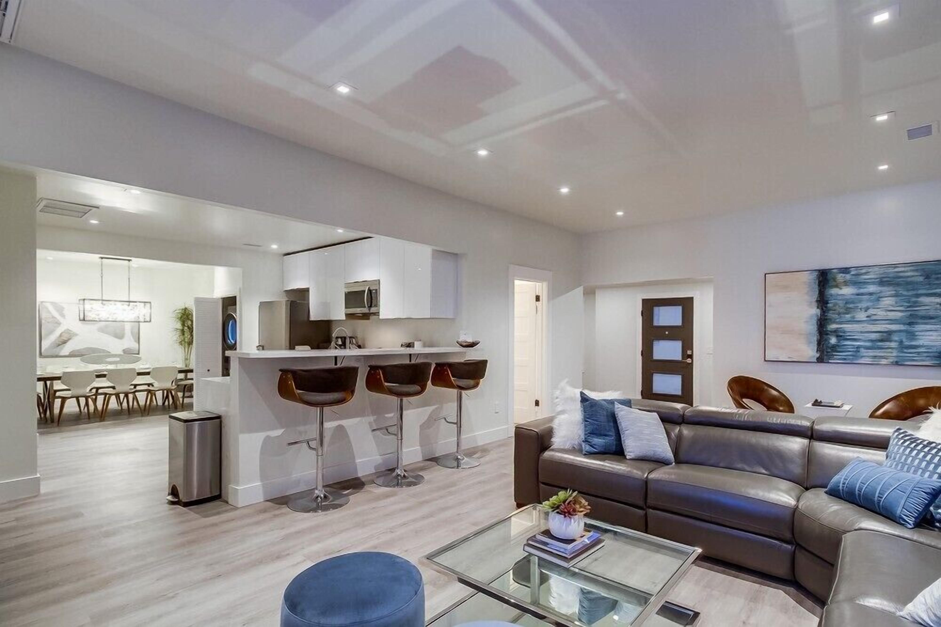 A modern living room with a sofa, coffee table, and a dining area with chairs and a kitchen in the background.