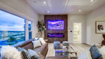 A modern living room with a large TV mounted on a wall, a comfortable sofa, a coffee table, and a view of the city through large windows.