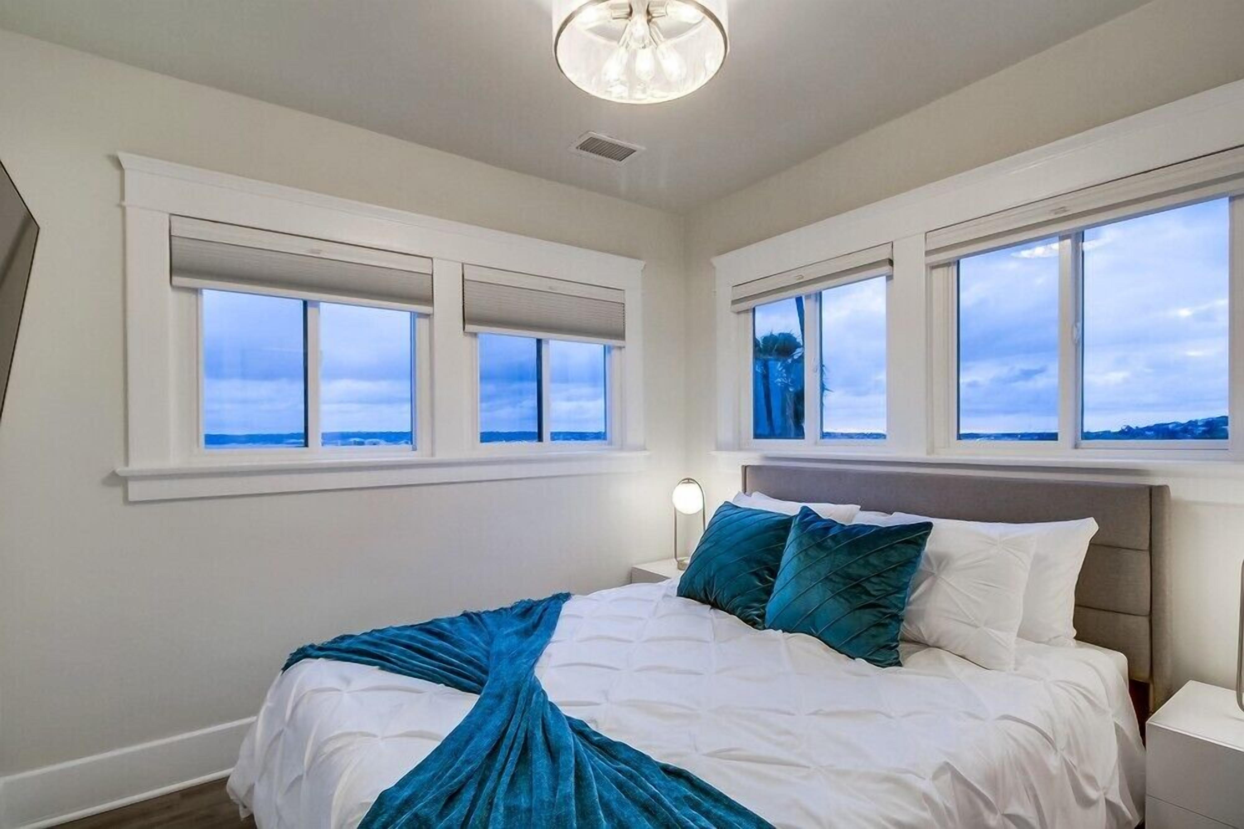 A bedroom with a bed, nightstands, and large windows with blinds.