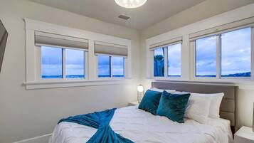 A bedroom with a bed, nightstands, and large windows with blinds.
