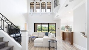 A spacious living area with a staircase, a large window, and a kitchen area.