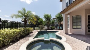 A swimming pool with a curved design, surrounded by a paved walkway and a black metal fence.