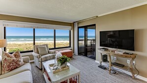 A spacious living room with a large TV, comfortable seating, a coffee table, and a view of the beach. - Oceanfront | Private Covered Balcony | Beautiful 4th Floor Amelia Surf and Racquet Condo (Fernandina Beach)