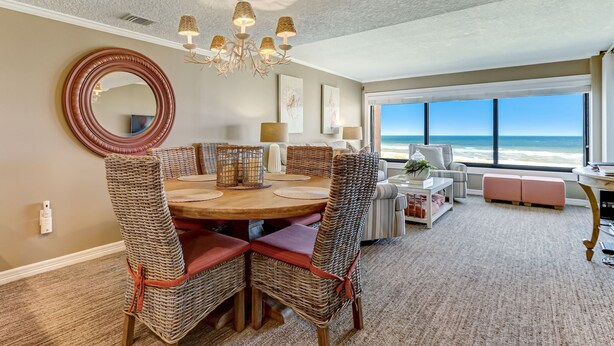 A dining area with a round table, wicker chairs, and a chandelier. - Oceanfront | Private Covered Balcony | Beautiful 4th Floor Amelia Surf and Racquet Condo (Fernandina Beach)