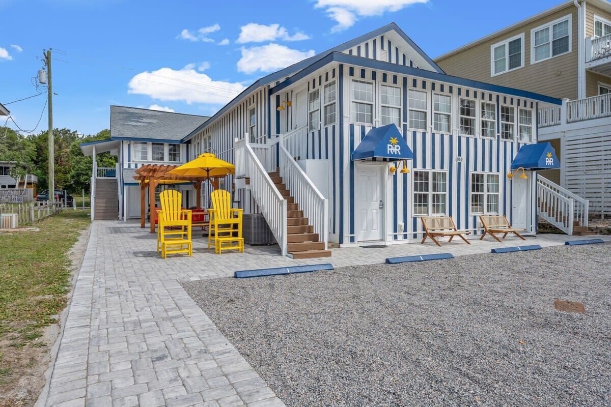 A building with a blue and white exterior, a covered outdoor seating area with yellow chairs, and a staircase leading to the entrance.