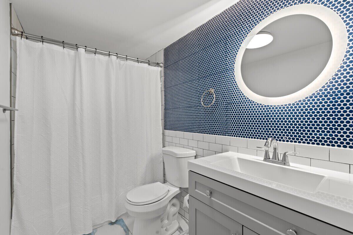 A bathroom with a white toilet, a white sink, and a mirror with a blue mosaic backsplash.