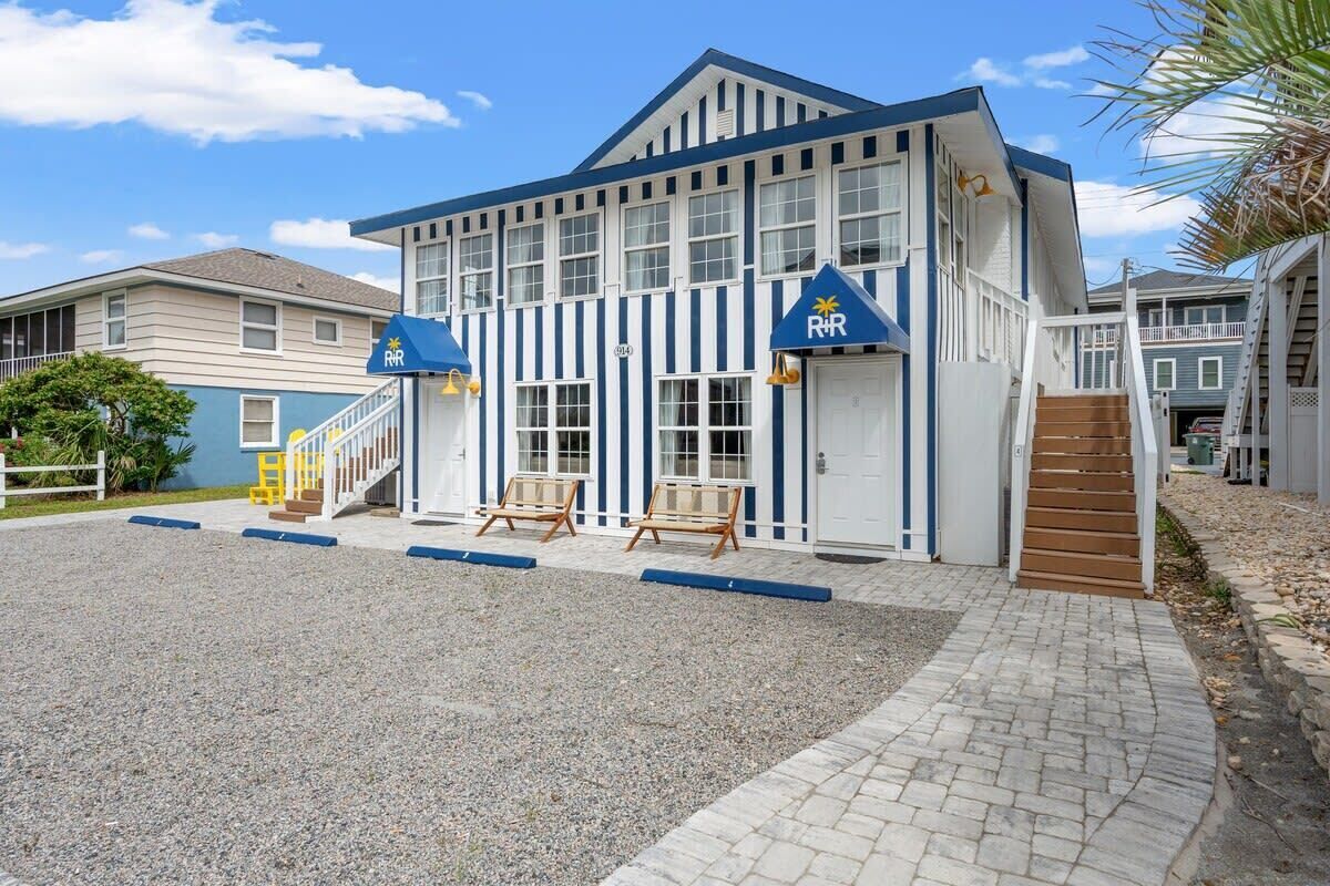 Ein Gebäude mit einer blau-weißen Fassade, einem überdachten Eingang mit einer Rampe und einer Treppe, die zu einem zweiten Stock führt.