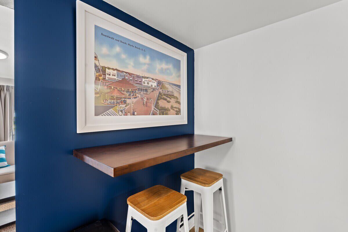 A framed coastal town map on a wall, a wooden shelf, and two white stools.