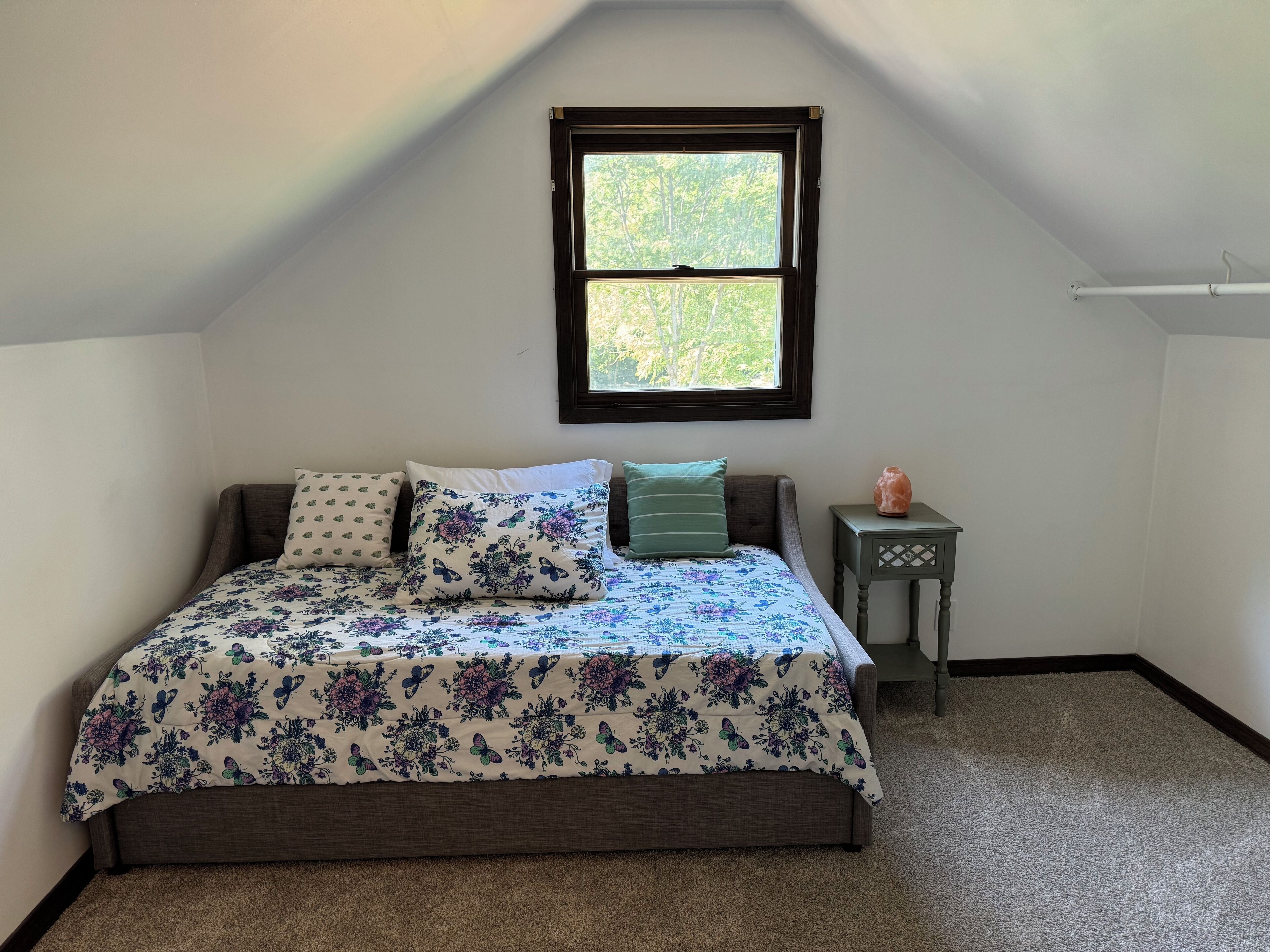 A bedroom with a bed, a window, a nightstand, and a heater.