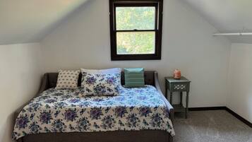 A bedroom with a bed, a window, a nightstand, and a heater.