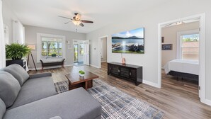 A spacious living room with a gray sofa, a coffee table, a black entertainment unit, and a large painting on the wall.