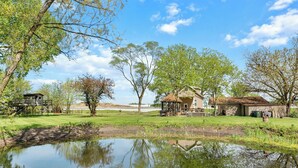 A rural landscape with a pond reflecting trees and a wooden structure.
