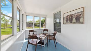 A bright room with a table and chairs, large windows, and a framed picture on the wall.